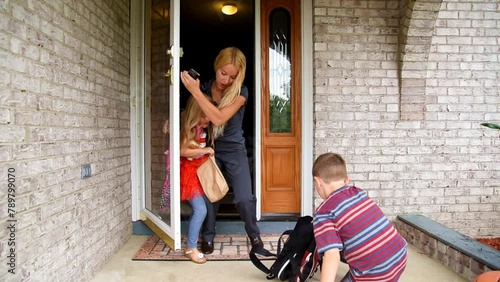 A mother is trying to leave the house talking on a phone with 2 children who are unprepared and dropping their book bags for school for a family stress, schedule or career concept.