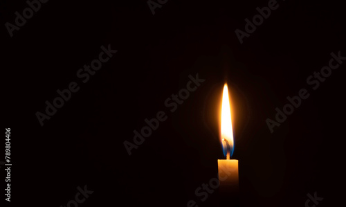 A single burning candle flame or light glowing on small orange candle on black or dark background on table in church for Christmas, funeral or memorial service with copy space