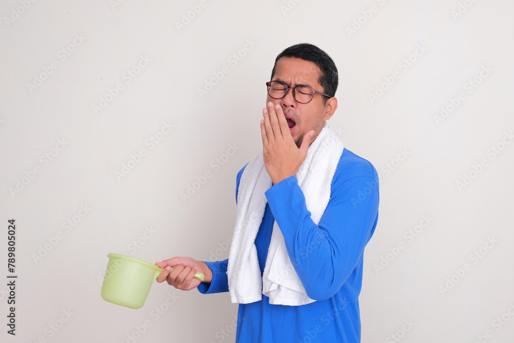 A man with towel around his neck and holding bath dipper yawning sleepy A man with towel around his neck and holding bath dipper yawning sleepy