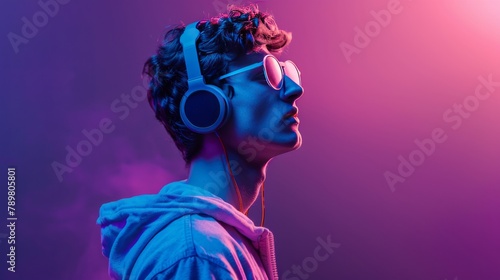 Portrait of a young man with curly hair listening to music with headphones and sunglasses on a pink and blue background