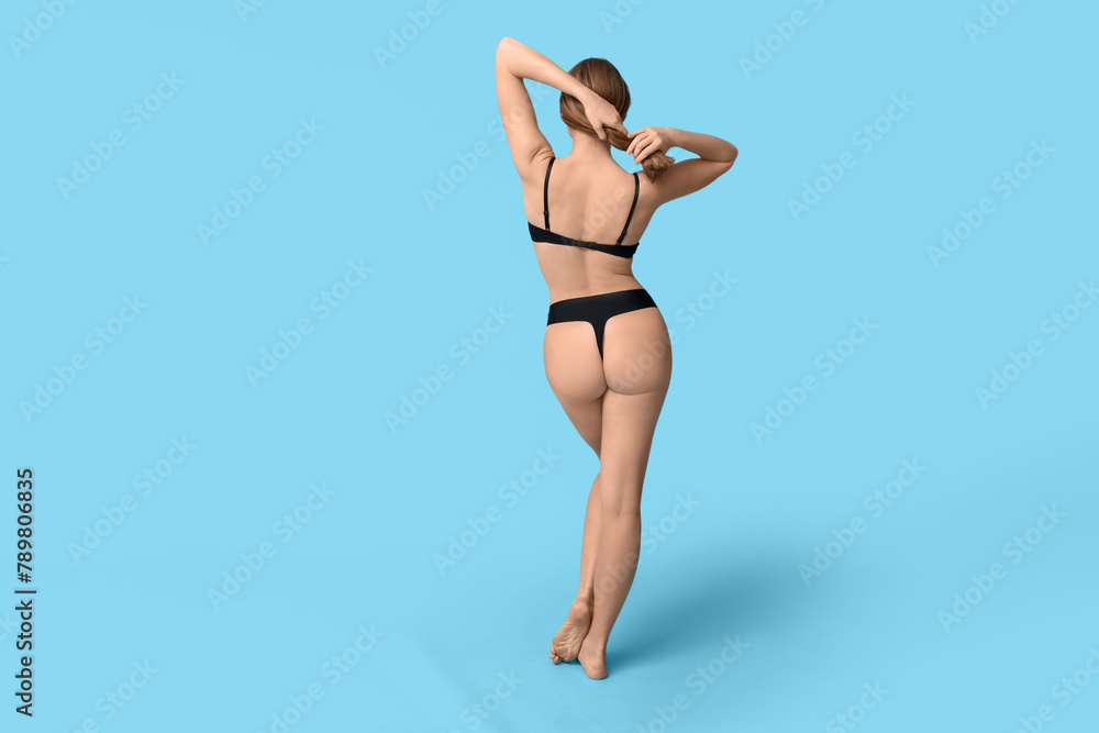 Attractive young woman in black underwear on blue background, back view Attractive young woman in black underwear on blue background, back view