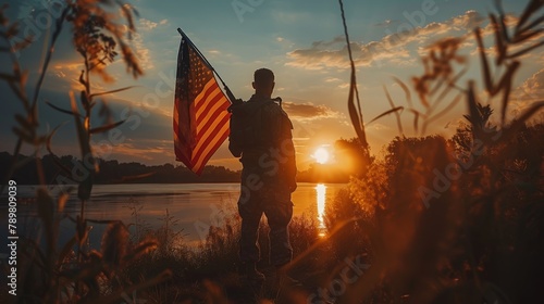 A soldier stands holding an American flag at sunset. photo