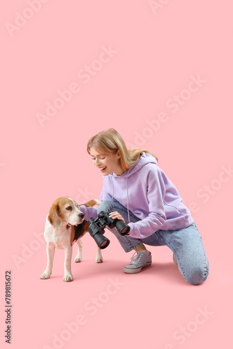 Young woman with binoculars and Beagle dog on pink background