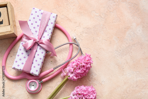 Stethoscope with gift box and flowers for International Nurses Day on beige grunge background