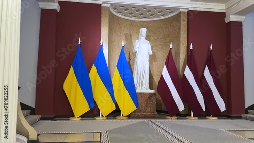 Riga, Latvia - April 4, 2024 - National flags in a classical interior with a statue between them, possibly in a governmental or cultural building. photo