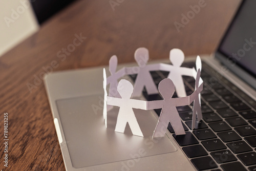 internet community concept, group of people online, circle of paper humans standing together and holding hands on laptop keyboard