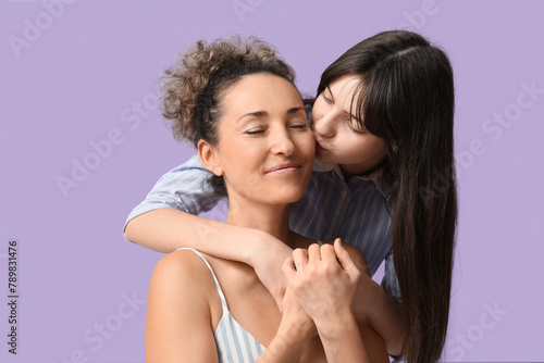 Teenage girl kissing her mature mother on lilac background