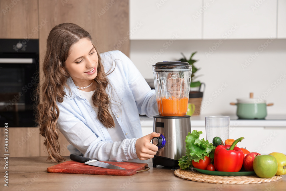 Beautiful young woman with blender making smoothie in kitchen