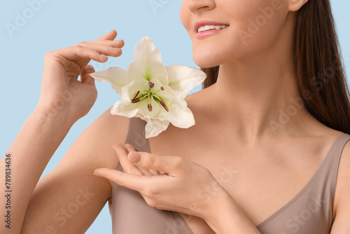 Beautiful young happy woman in underwear with white lily flower on blue background, closeup