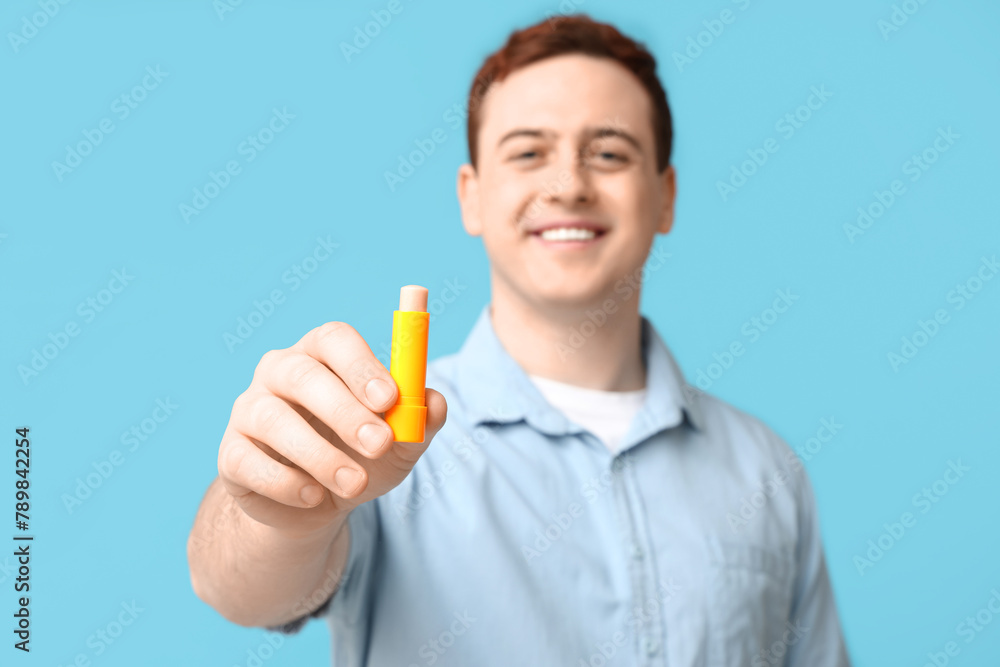 Happy young man with lip balm on blue background Happy young man with lip balm on blue background