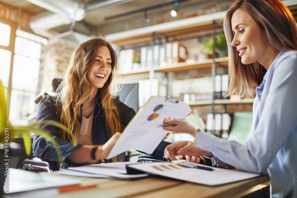 Two smiling businesswomen discussing data analysis with charts and reports at desk. Two smiling businesswomen discussing data analysis with charts and reports at desk.