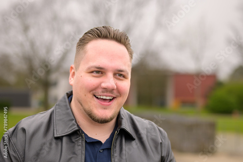 Portrait of a young man standing outside in a park in spring and looking friendly to side