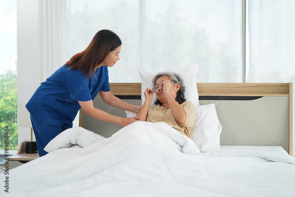 Young Caregiver female take senior woman go to sleep on bed in bedroom Young Caregiver female take senior woman go to sleep on bed in bedroom