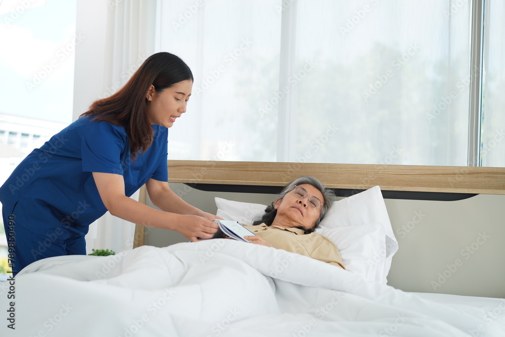 Obraz premium Young Caregiver female take senior woman go to sleep on bed in bedroom