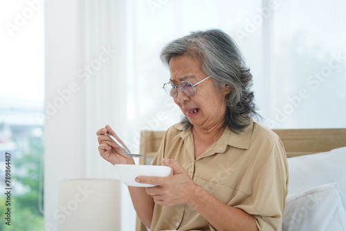 Senior woman wearing glasses sitting on bed hold a bowl with feeling anorexic photo