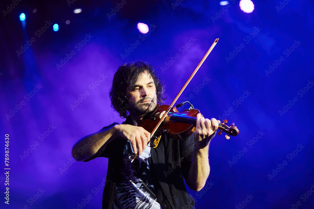 Fototapeta premium A violinist musician stands on stage with a violin in his hands during a concert. There is a bright light from the floodlights around.