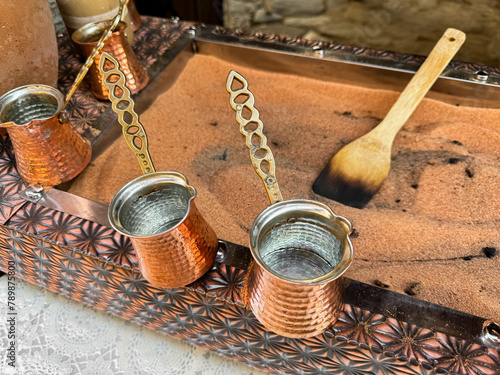 Traditional Turkish coffee in copper turks with long handles on tray with sand. Real coffee preparation, close up with selective focus.