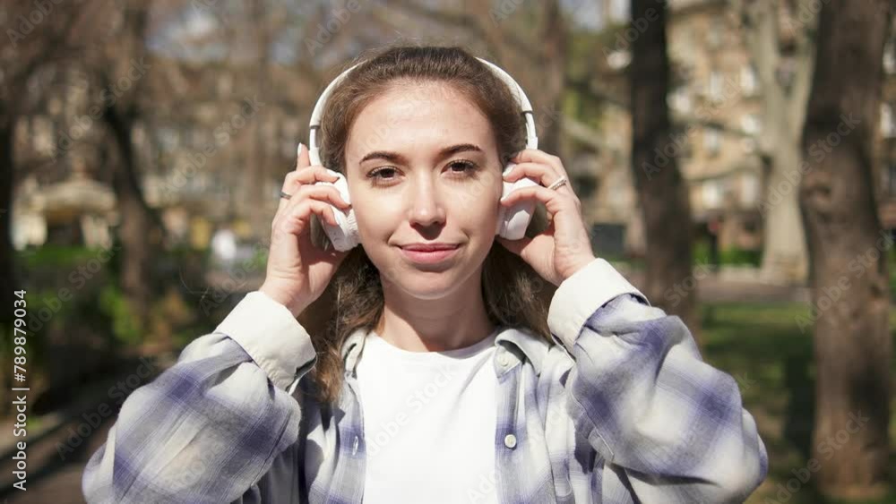 Young blonde woman in checkered shirt looking to the camera, smiling and putting on headphones Young blonde woman in checkered shirt looking to the camera, smiling and putting on headphones