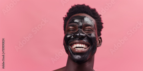 African-American shocked man with clay facial mask and towel on head uses beauty products and cosmetic on blue studio background. Copy paste empty place for text. Skin care and peeling concept