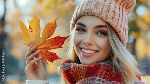 Beautiful young happy woman with a bright red-yellow autumn leaf in the park.