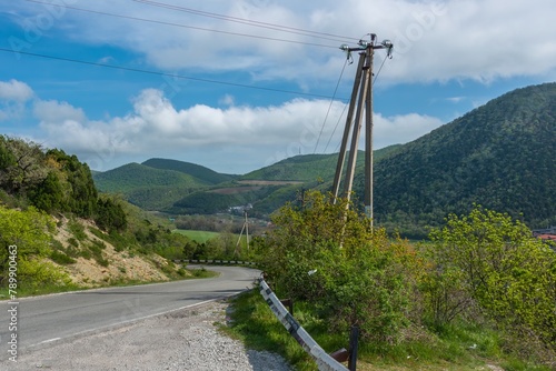 winding asphalt road and power line support in the green forested mountains of the Western Caucasus near the village of Abrau (South Russia) on a sunny spring day