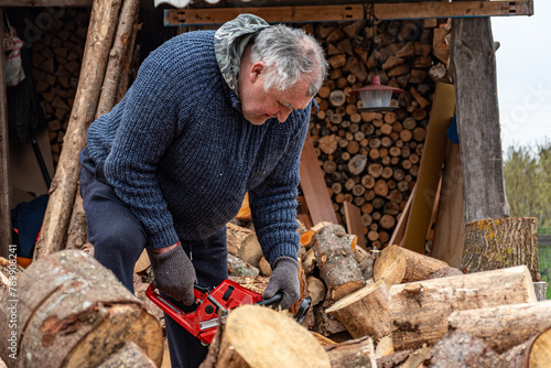 A man works with a saw, processing firewood for the winter season
