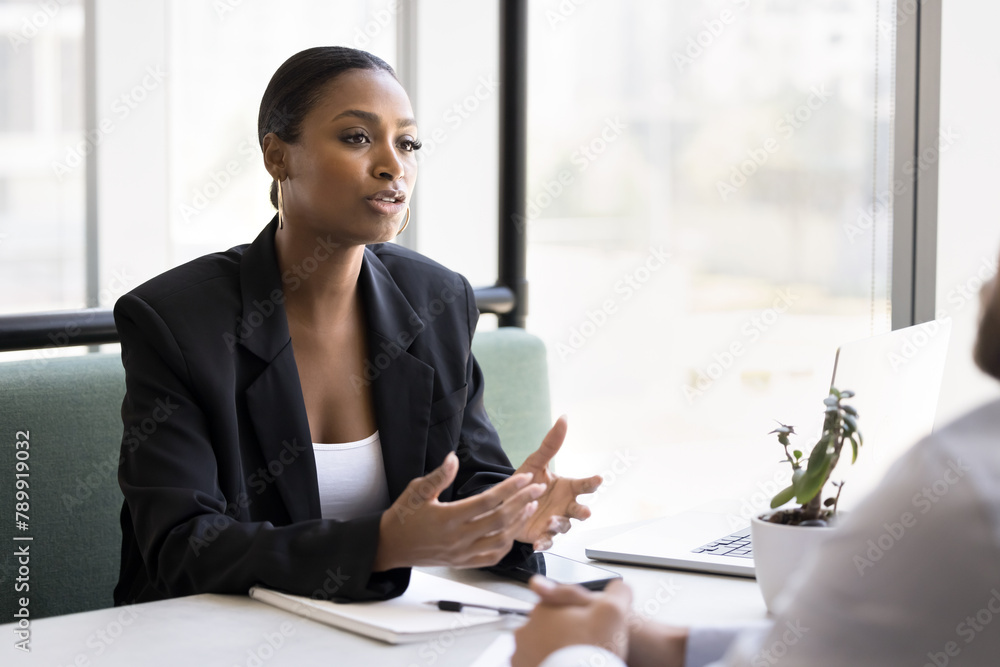 Serious beautiful African American consultant woman talking to customers at business meeting, sitting at cafe table, speaking. Real estate agent, bank broker, financial advisor giving consultation Serious beautiful African American consultant woman talking to customers at business meeting, sitting at cafe table, speaking. Real estate agent, bank broker, financial advisor giving consultation