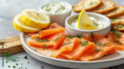 A white plate holds sliced salmon, cream cheese in a bowl, and lemon wedges