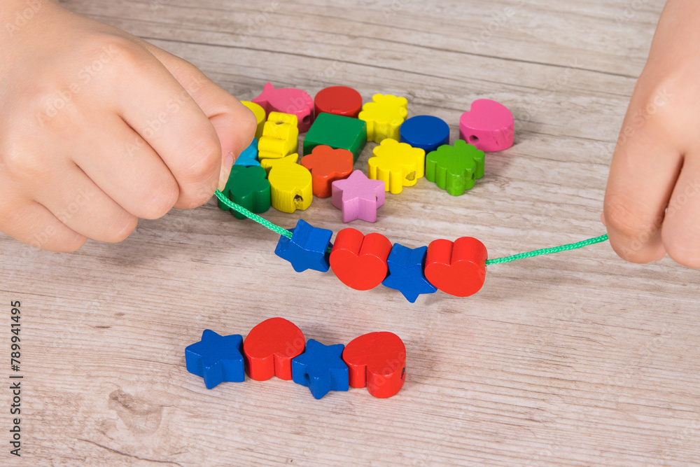 Preschooler making bracelet from thread and wooden colored beads ...