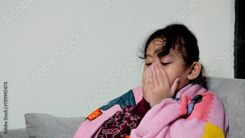 A young girl is sitting on a couch with a blanket wrapped around her.
