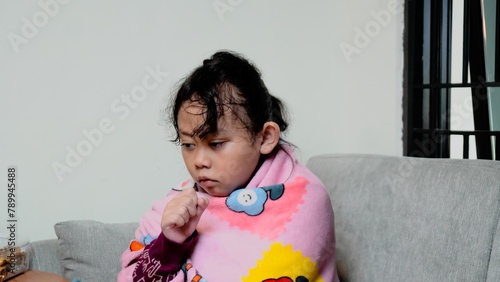 A young girl is sitting on a couch with a blanket wrapped around her.