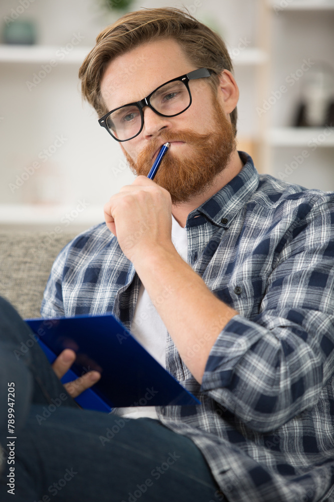 contemplative man sat on sofa holding a notebook contemplative man sat on sofa holding a notebook