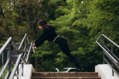 Young attractive woman in sportswear doing a warm-up on stairs before training outdoor in summer day.. Workout, sport, activity, fitness, vacation and training concept. © Roman