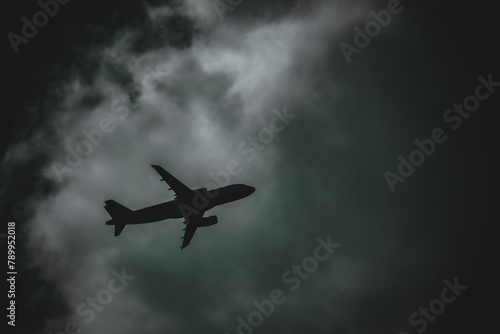 Jet aircraft silhouetted in a night sky flying through a gap in the clouds