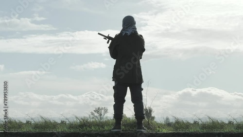 war watchman terrorist standing holding rifle outdoor,rebel soldier separatist guard with gun stands at the vantage point watching out for enemy back view photo