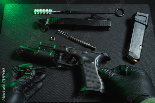 Cleaning and repairing weapons. Hands of a gunsmith and a disassembled pistol in a workshop. photo