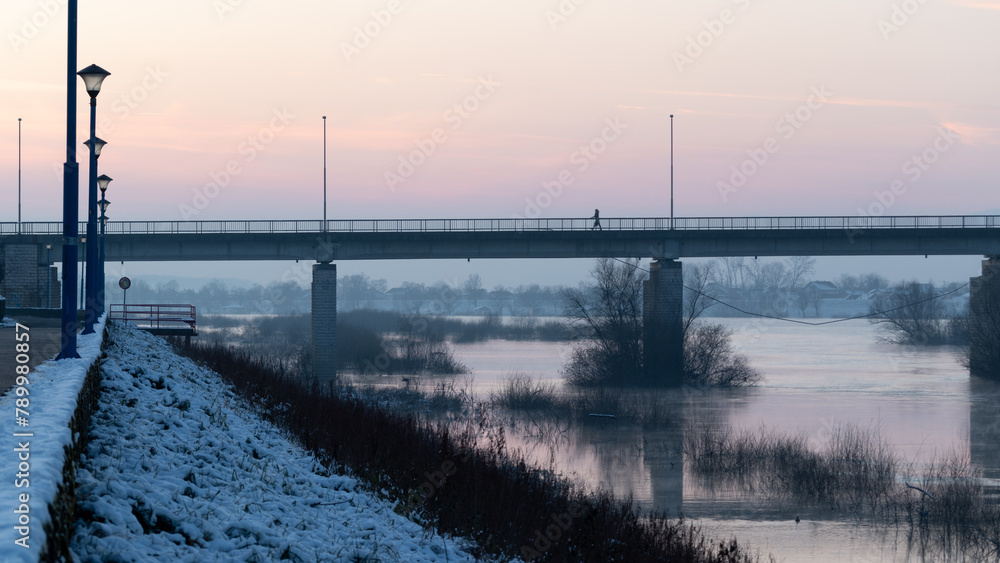One person walks across bridge during twilight, winter landscape of Sava river