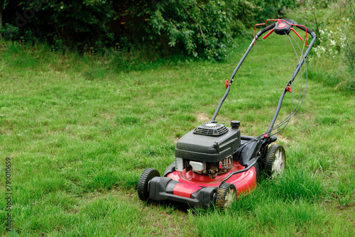 Lawn mover on green grass background. Machine for cutting lawns. Garden care. Electric equipment. Side view. Copy space. Lots of clover weeds. Sport lawn field for games. Banner. High quality photo