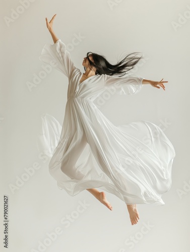 Woman in flowing white dress captured mid-leap against a pale background, embodying freedom and grace.