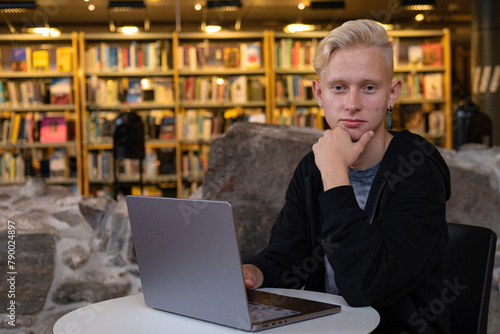 portrait of a young blond guy with a laptop. The boy student is smiling because he completed the task