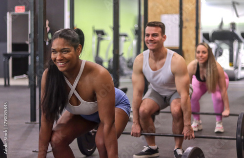 Group of multiracial smiling people doing dead lift with some bars with discs inside a gym, front view, sport dress. Fitness and healthy lifestyle concept