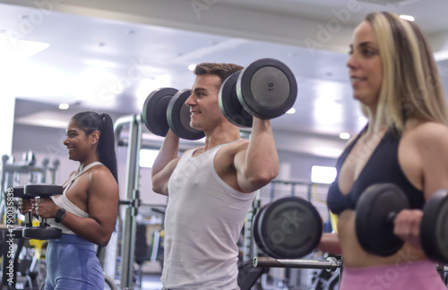 Multiracial smiling couple exercising their arms with dumbbells in a gym. Fitness and healthy lifestyle concept