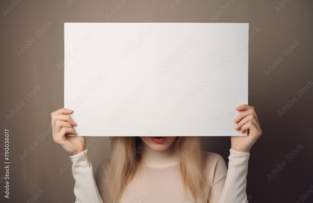 A woman holding a blank white poster in front of her face. Empty paper banner in girls hands, she hides behind it. A woman holding a blank white poster in front of her face. Empty paper banner in girls hands, she hides behind it.