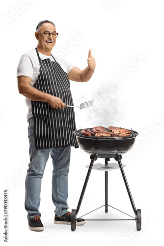 Mature man grilling meat on a barbecue and gesturing thumbs up