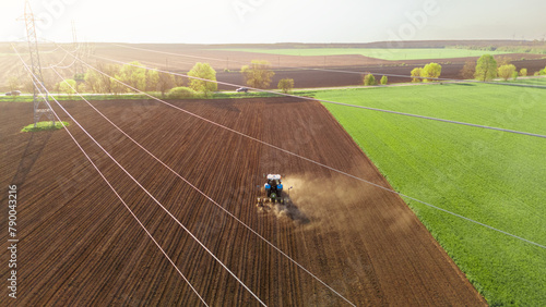Tractor plows field in the spring. Aerial top view, power line in the foreground