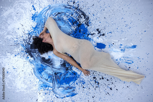 sexy young nude woman in white transparent cotton stocking dress, lies on the artistically designed floor with colorful splashes of paint in the artists studio