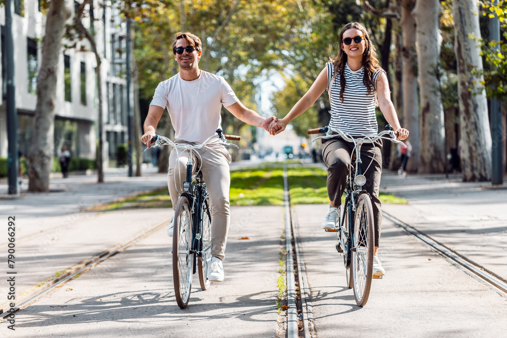 Happy loving couple cycling while holding each other hand in the city