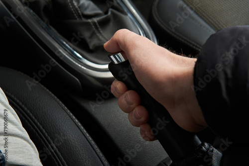 Man holding and pulling handbrake handle emergency parking e-brake in the black car interior
