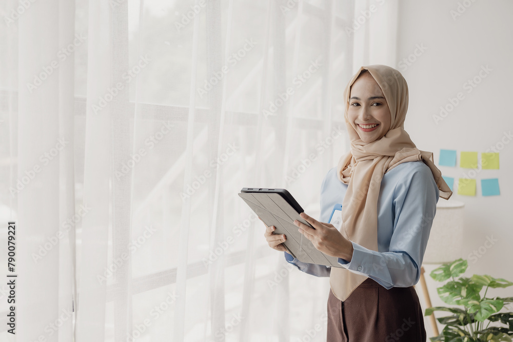Asian Muslim businesswoman uses calculator and writes notes with mathematical financial calculations on table at office with laptop and financial documents, taxes, accounting, financial Asian Muslim businesswoman uses calculator and writes notes with mathematical financial calculations on table at office with laptop and financial documents, taxes, accounting, financial