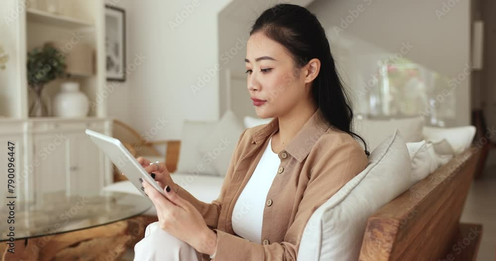 Asian woman sit on sofa using tablet choose goods, make order, purchase services via marketplace, lead chat, correspond to client working remotely from home. Modern technology, communication, commerce Asian woman sit on sofa using tablet choose goods, make order, purchase services via marketplace, lead chat, correspond to client working remotely from home. Modern technology, communication, commerce